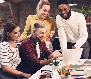 Imagem com quatro pessoas sorrindo e olhando para a tela de um computador